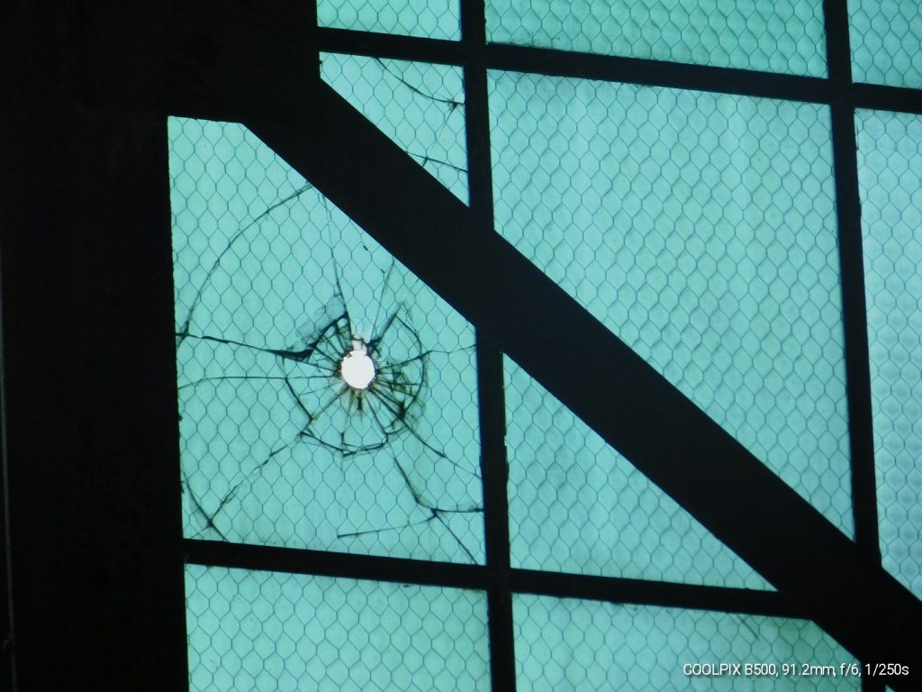 Poignant image of a bullet hole in a hangar window on Ford Island