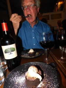 Tom enjoying his lava cake, with a bottle and a glass of red wine on the table in front of him