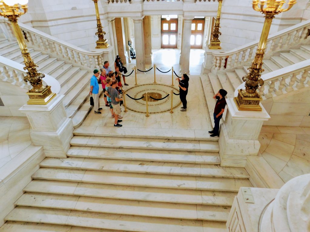 People standing on the rotunda, circling the state weapon. Two side stairs coming down to them, one stairway in the front going down from them.  