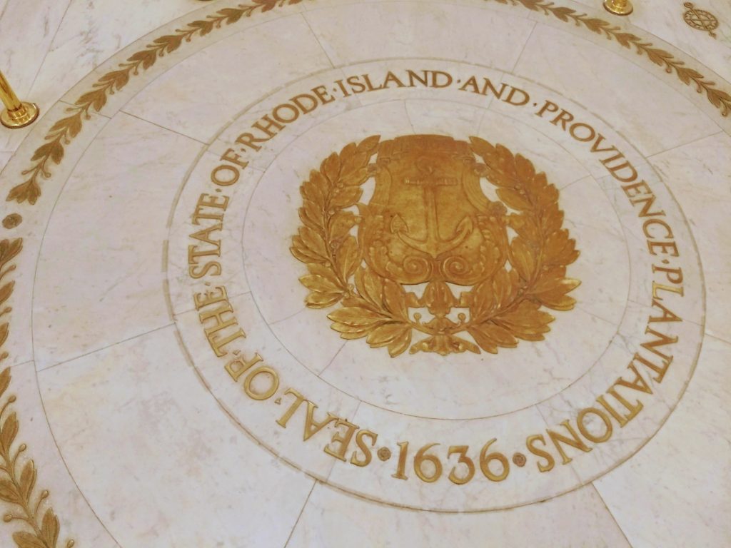 The 1636 Seal of  the State of Rhode Island and Providence Plantations. In the center is an anchor with the word "Hope"