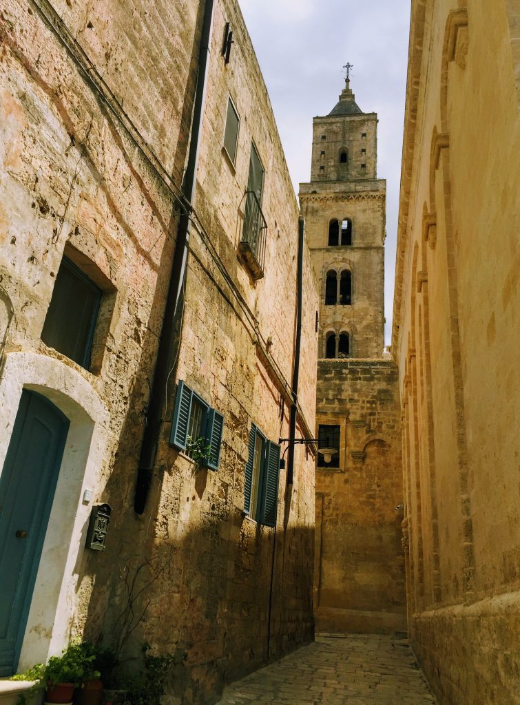 Walking through narrow streets towards the Matera Cathedral clock tower 