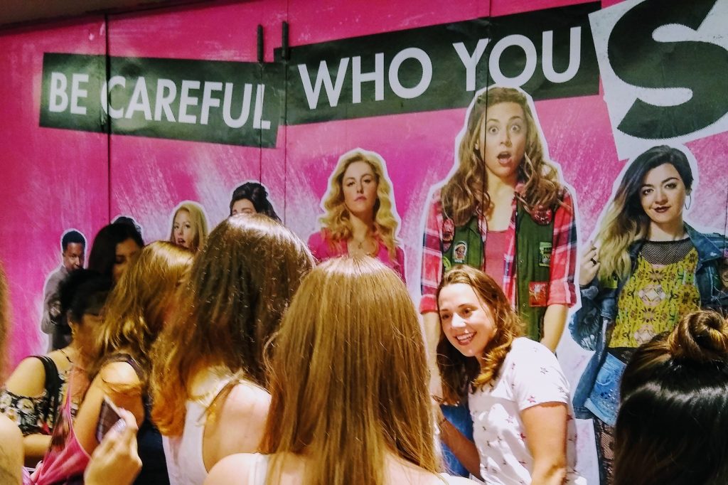 Teens in front of "Be Careful Who You Sit With" poster talking to one of the actors