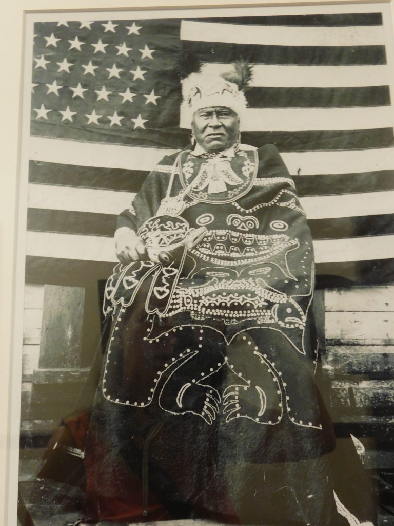 Native Alaskan Tlingit chief in front of the American flag. You can find many interesting facts about the Alaskan natives in the Alaska Capitol