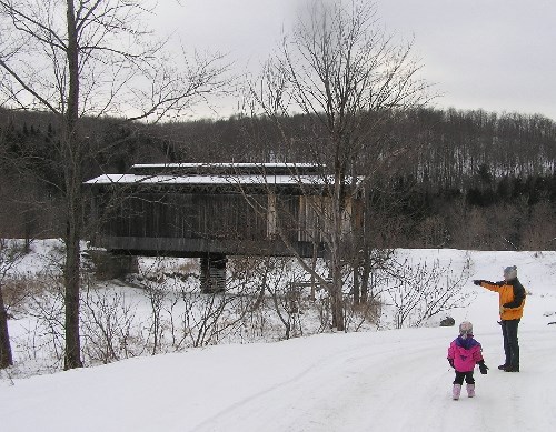 Two geocachers with a covered bridge in the snow