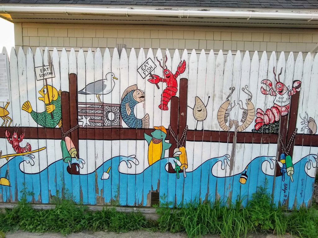 Mural on a gate with fish holding "Eat Lobster!" and lobster holding "Eat Fish!" sign, joined by lobster with "Got Lobstah?" bib.
Can be found in Cape Porpoise, Maine
So many cool things to do in Kennebunkport!