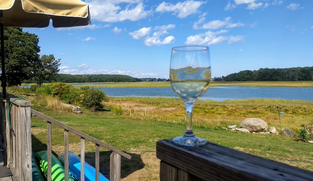 White wine glass on railing looking out over Kennebunkport Little River next to Goose Rocks Beach.