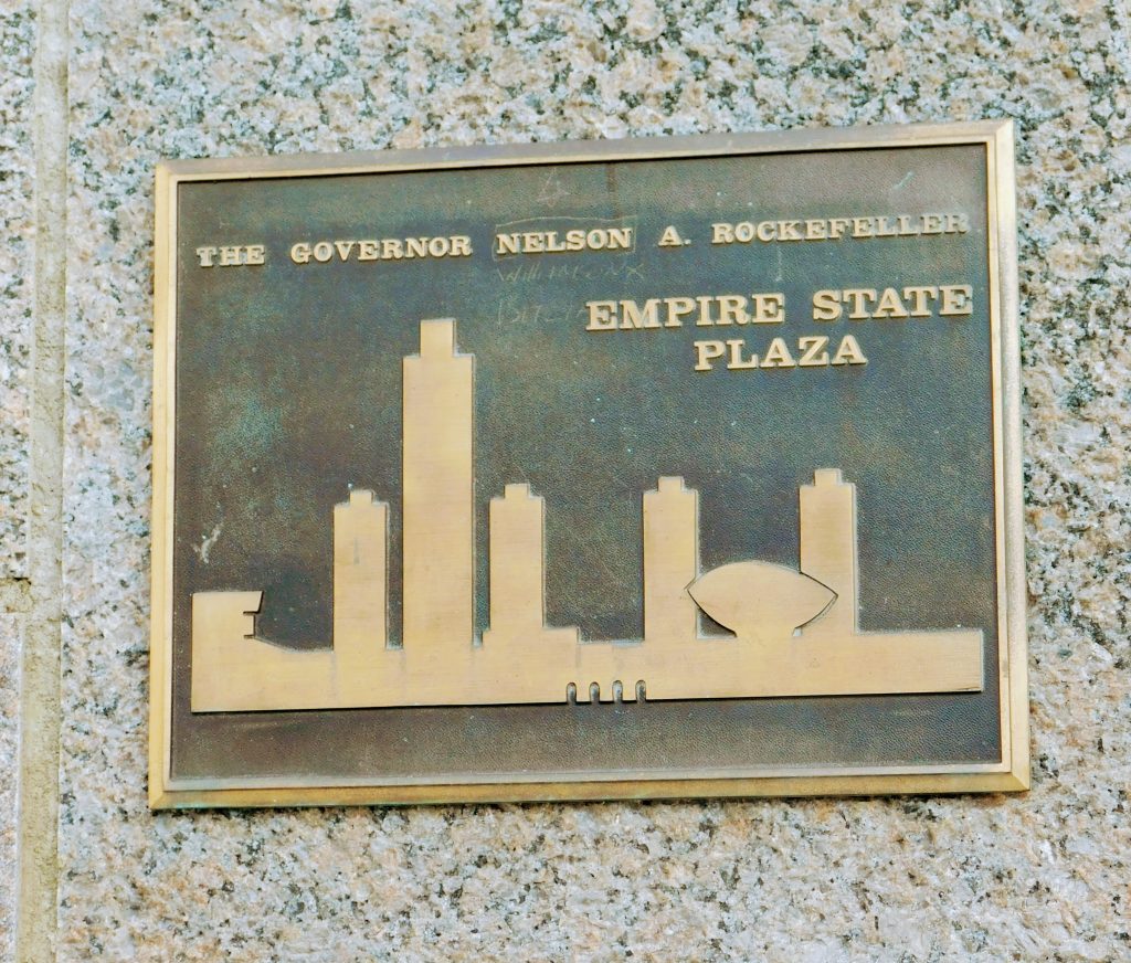 Plaque honoring The Governor Nelson A. Rockefeller and the EMPIRE STATE PLAZA with an abstract view of it. 
