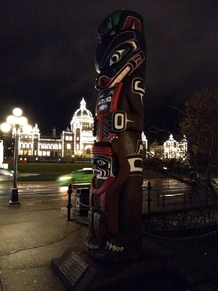 Totem pole in Victoria BC, with parliament building in the background. Taken at night. 