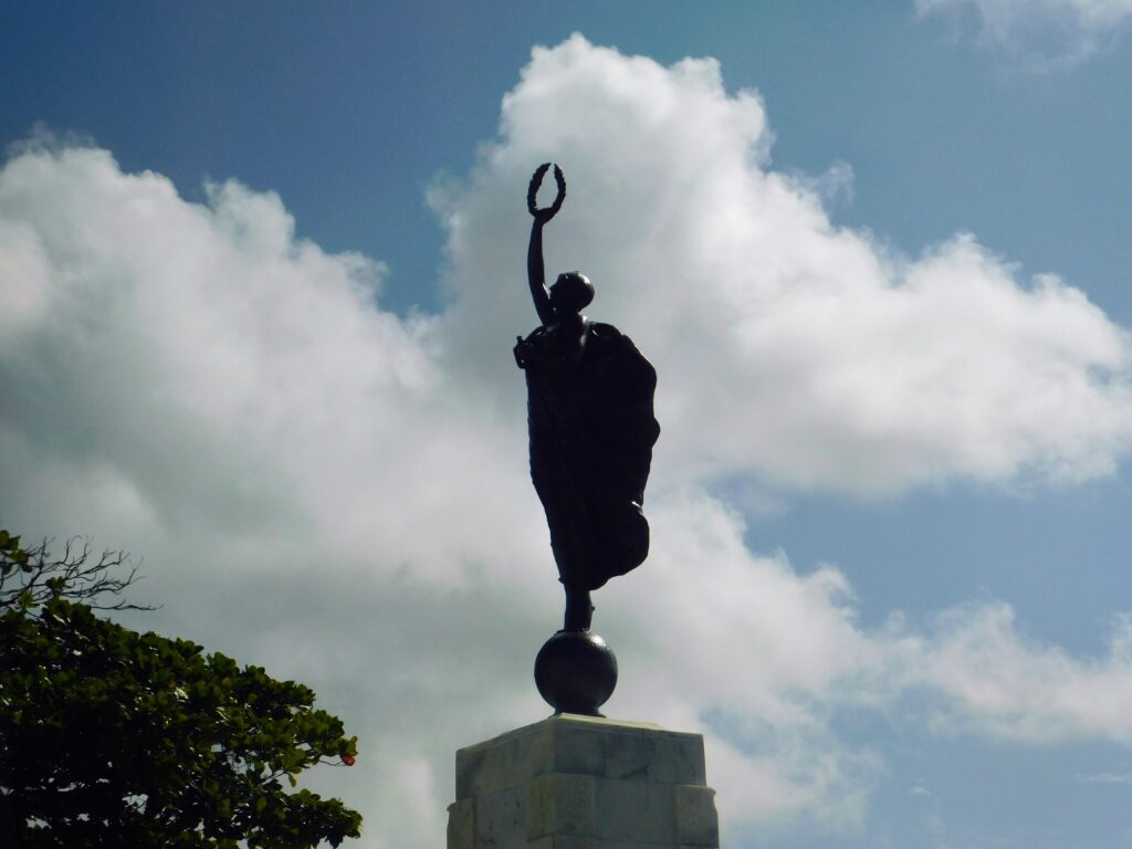 Statue in front of the Puerto Rico capitol. Figure holding a laurel wreath with sky / clouds in background