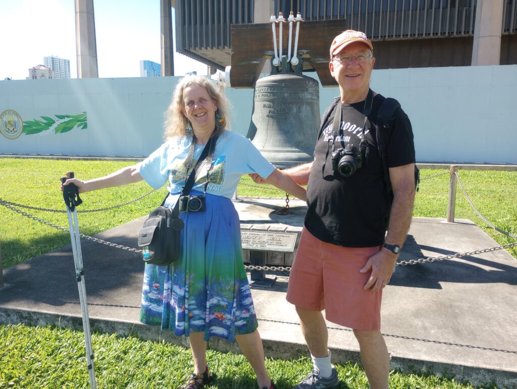 Karen and Tom, OurCawrpeDiem in front of the Hawaiian Cpitol and its full sized liberty bell replica. 